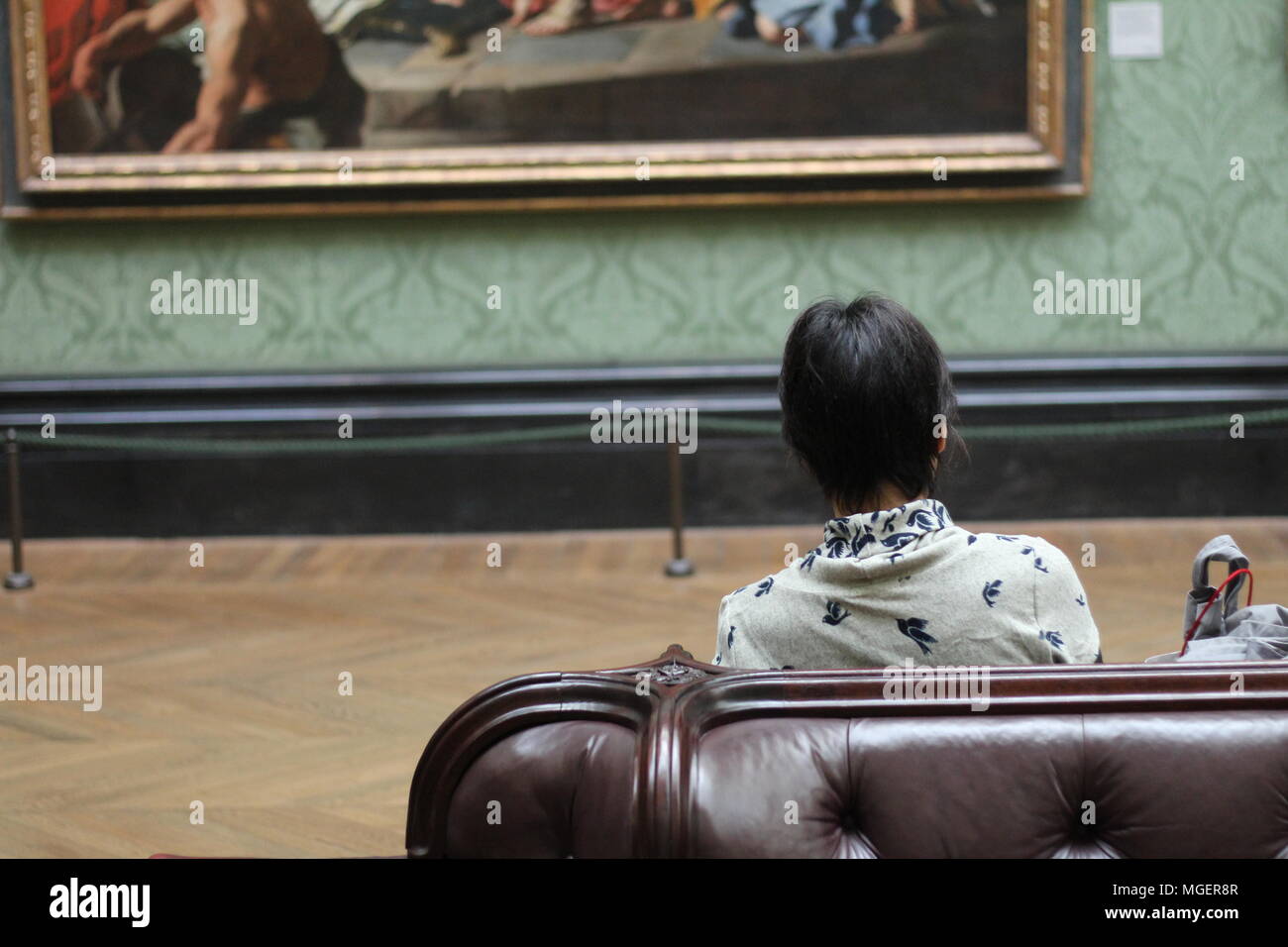 Una donna seduta su una poltrona di pelle di un museo, intenti ad ammirare un dipinto nella parte anteriore di esso Foto Stock