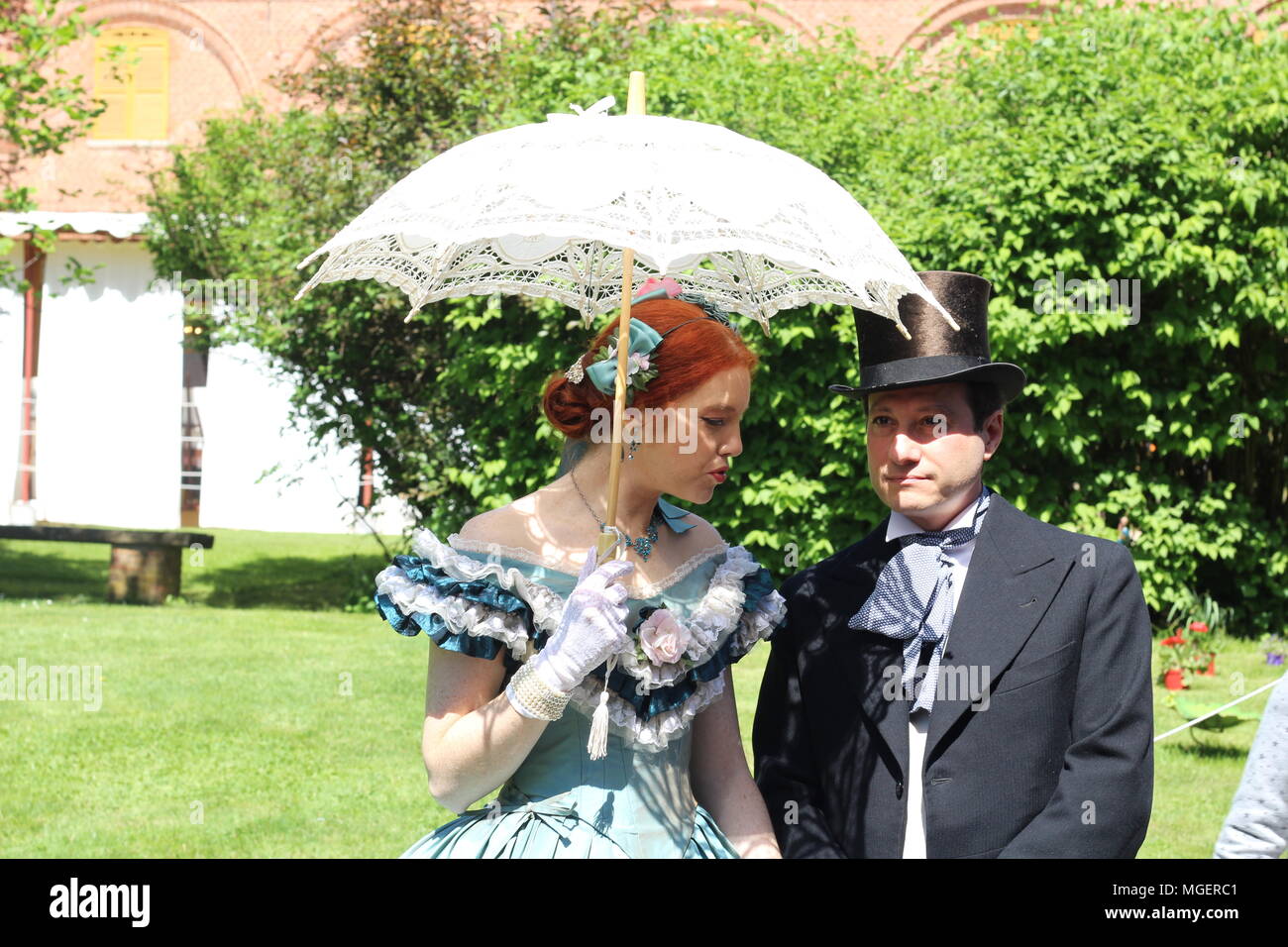 Una coppia di sposi vestito in abiti del passato mentre si sussurra qualcosa nel suo orecchio impassibile Foto Stock