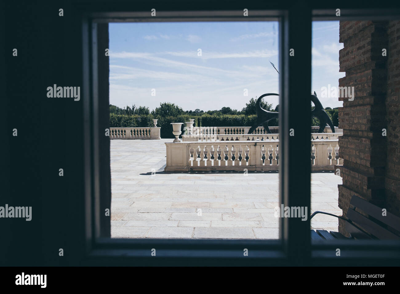 Una vista da una finestra di un palazzo di una terrazza bianca con ornamenti come vasi e opere d'arte che si affacciano su un giardino Foto Stock