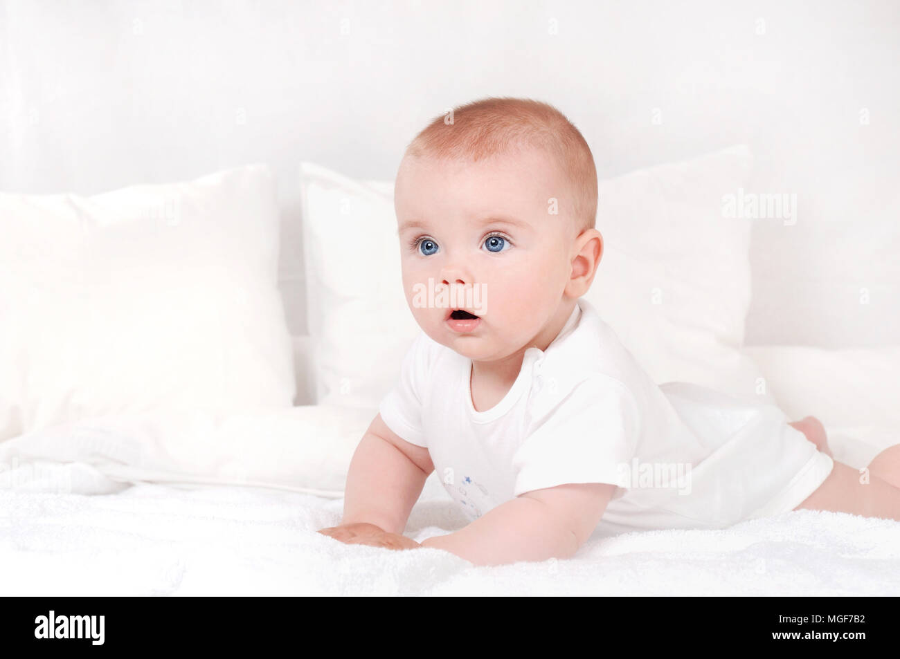 Bel ritratto di incredibile e affascinante piccolo bambino. Sorridenti bambino con gli occhi blu su bianco sullo sfondo del letto Foto Stock