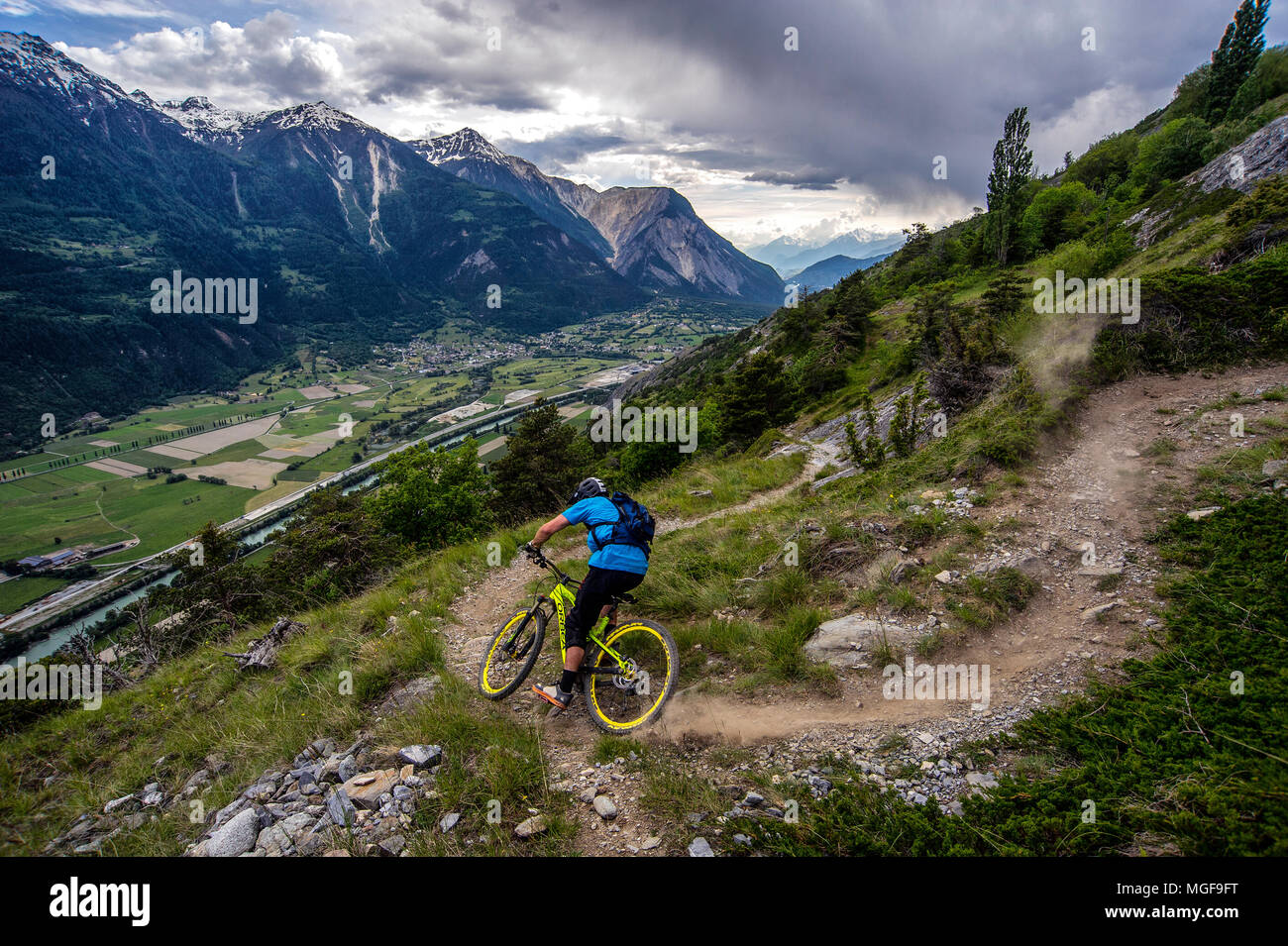Un uomo corse in mountain bike in alto sopra il piano della valle in prossimità della città di Gampel e Jeizinen in Vallese della Svizzera. Foto Stock