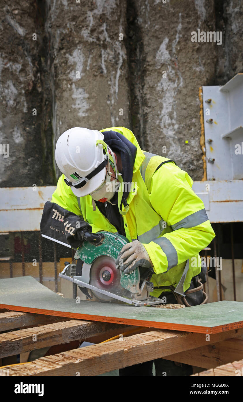 Un operaio (non identificabile) utilizza una sega circolare elettrica per tagliare il compensato in un cantiere edile a Londra. Foto Stock