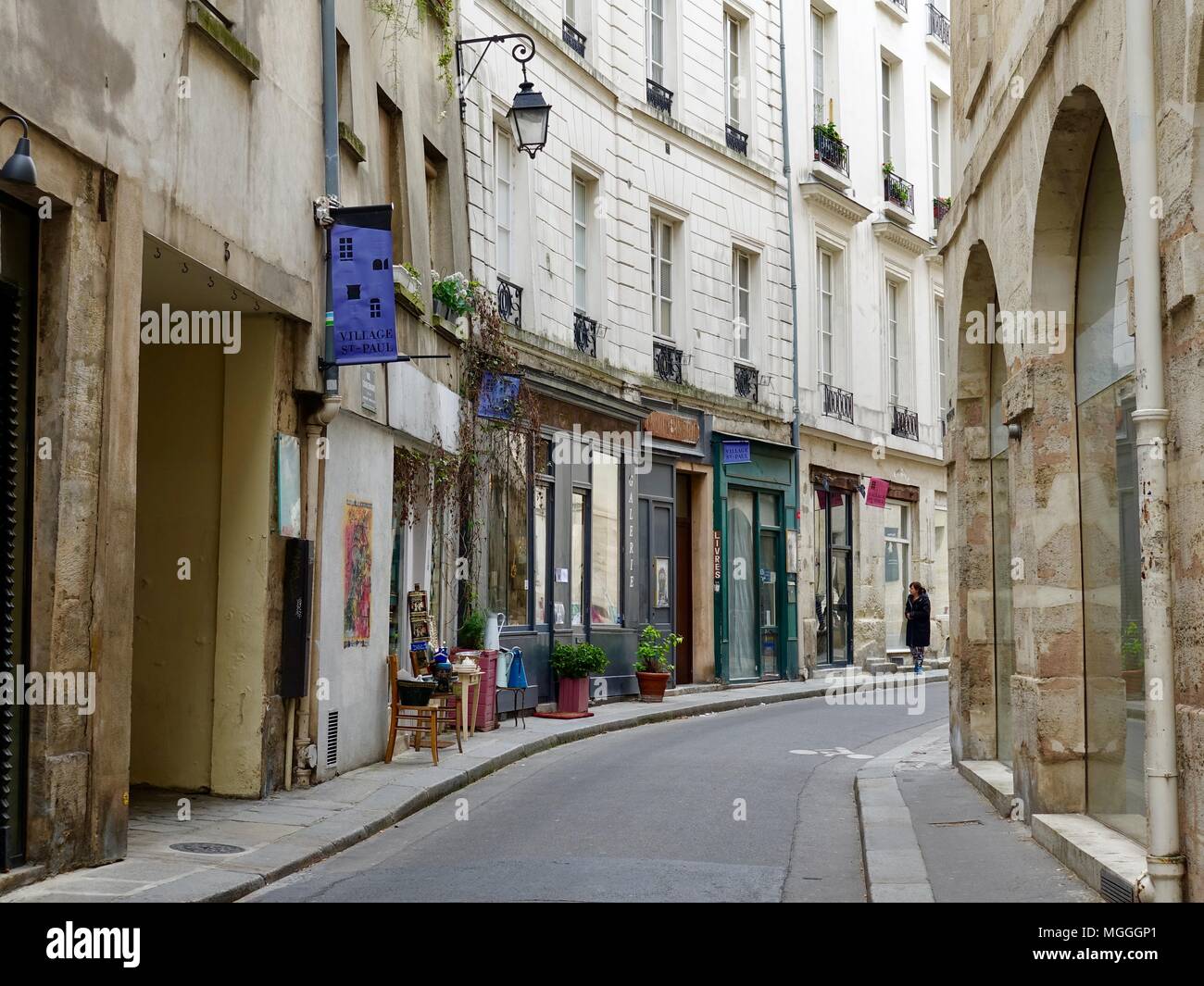 Lone donna camminando giù per una strada curva, passato negozi, nel villaggio di San Paolo quartiere del Marais. Parigi, Francia. Foto Stock