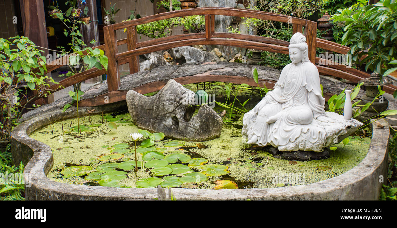 Signora Buddha che si affaccia su un laghetto con un white lotus bloom Foto Stock