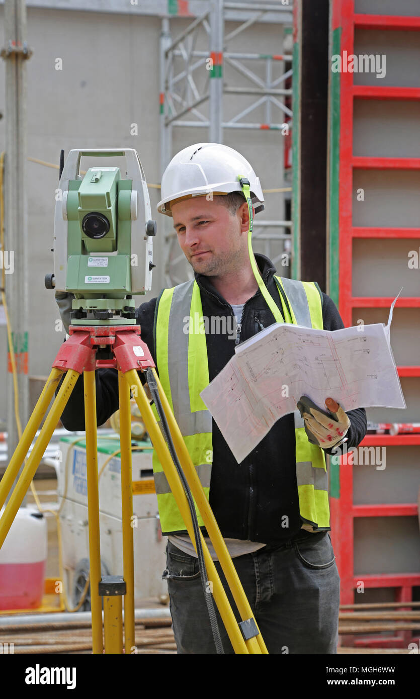 Una costruzione geometra aggiusta un livello elettronico su un grande Londra sito in costruzione. Mostra in acciaio maglia di rinforzo in background. Foto Stock