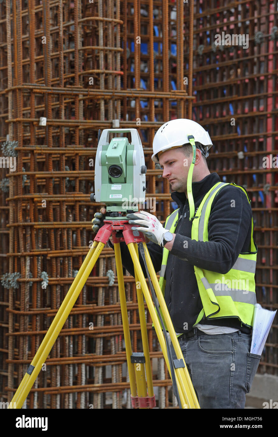 Una costruzione geometra aggiusta un livello elettronico su un grande Londra sito in costruzione. Mostra in acciaio maglia di rinforzo in background. Foto Stock