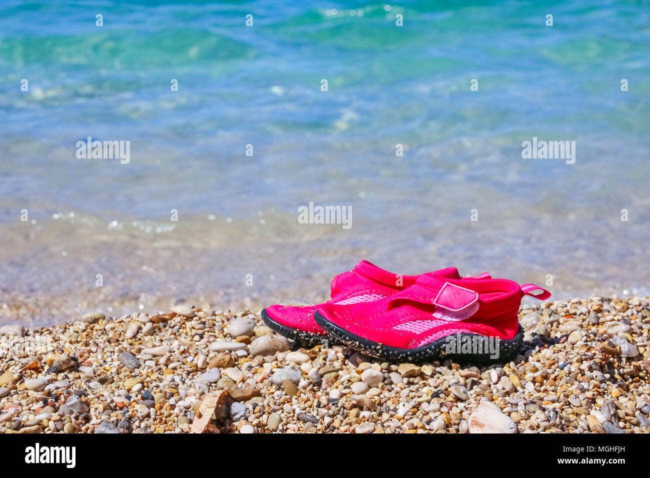 Coppia di rosa scarpe nuoto su marmo spiaggia ghiaiosa accanto all acqua del  mare turchese. Vacanze