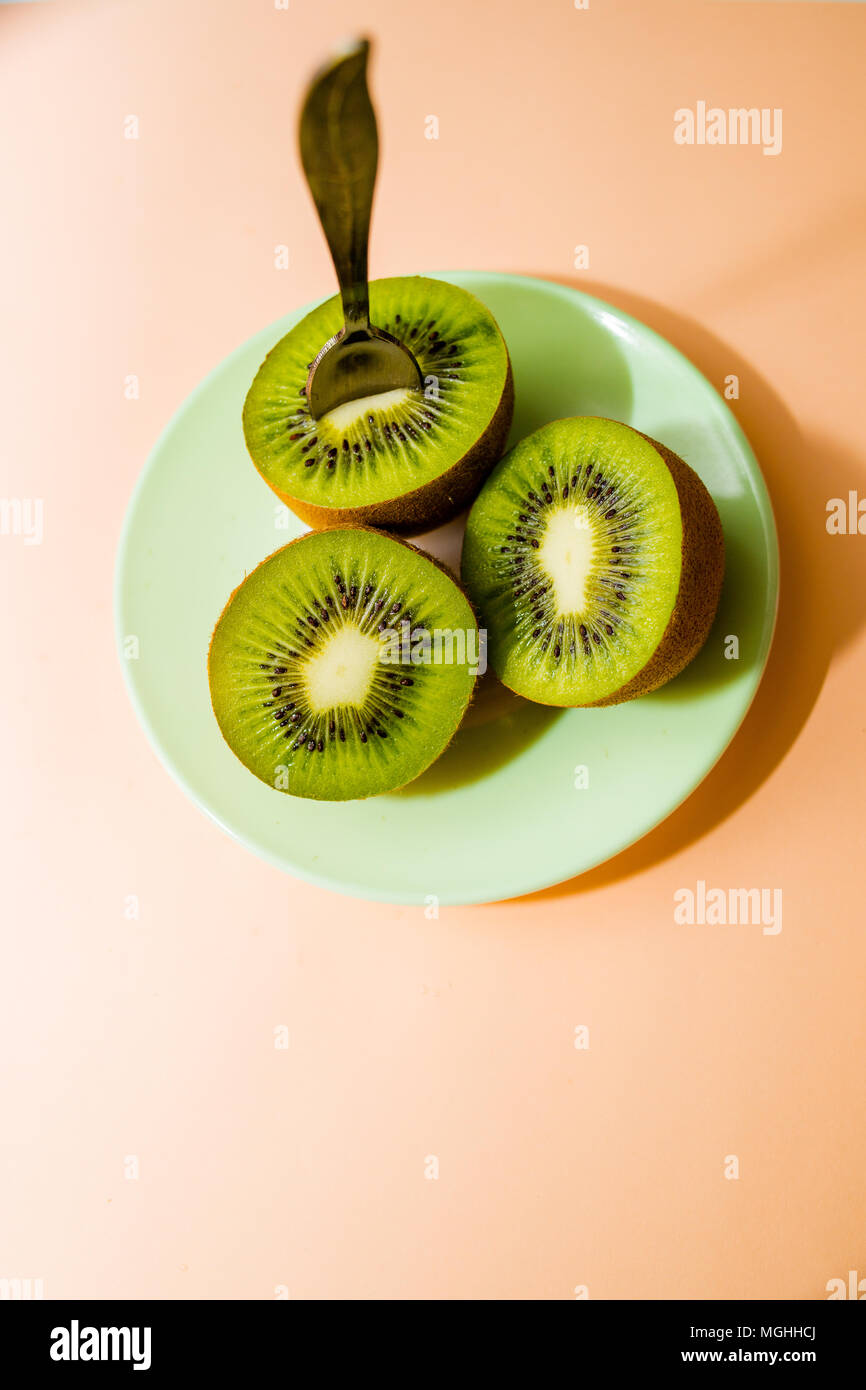 Kiwi isolata sulla piastra con il cucchiaio, su sfondo rosa. Taglio del dolce verde kiwi. Detox, perdita di peso, mangiare vegetariano. Dieta sana nozione. spazio copia Foto Stock