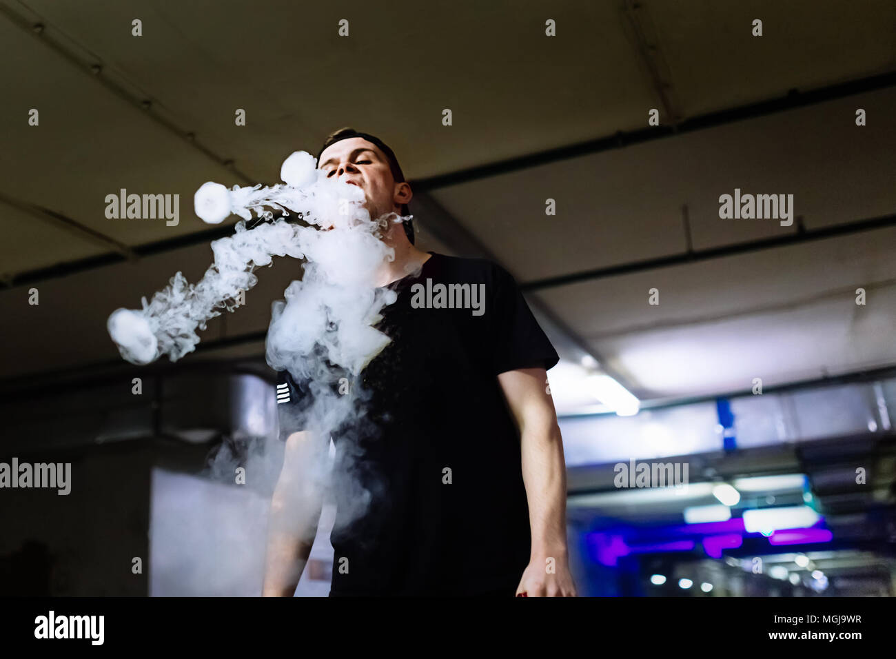 L uomo nel tappo un fumo di sigaretta elettronica e rilascia le nubi di vapore di eseguire vari tipi di vaping trucchi Foto Stock