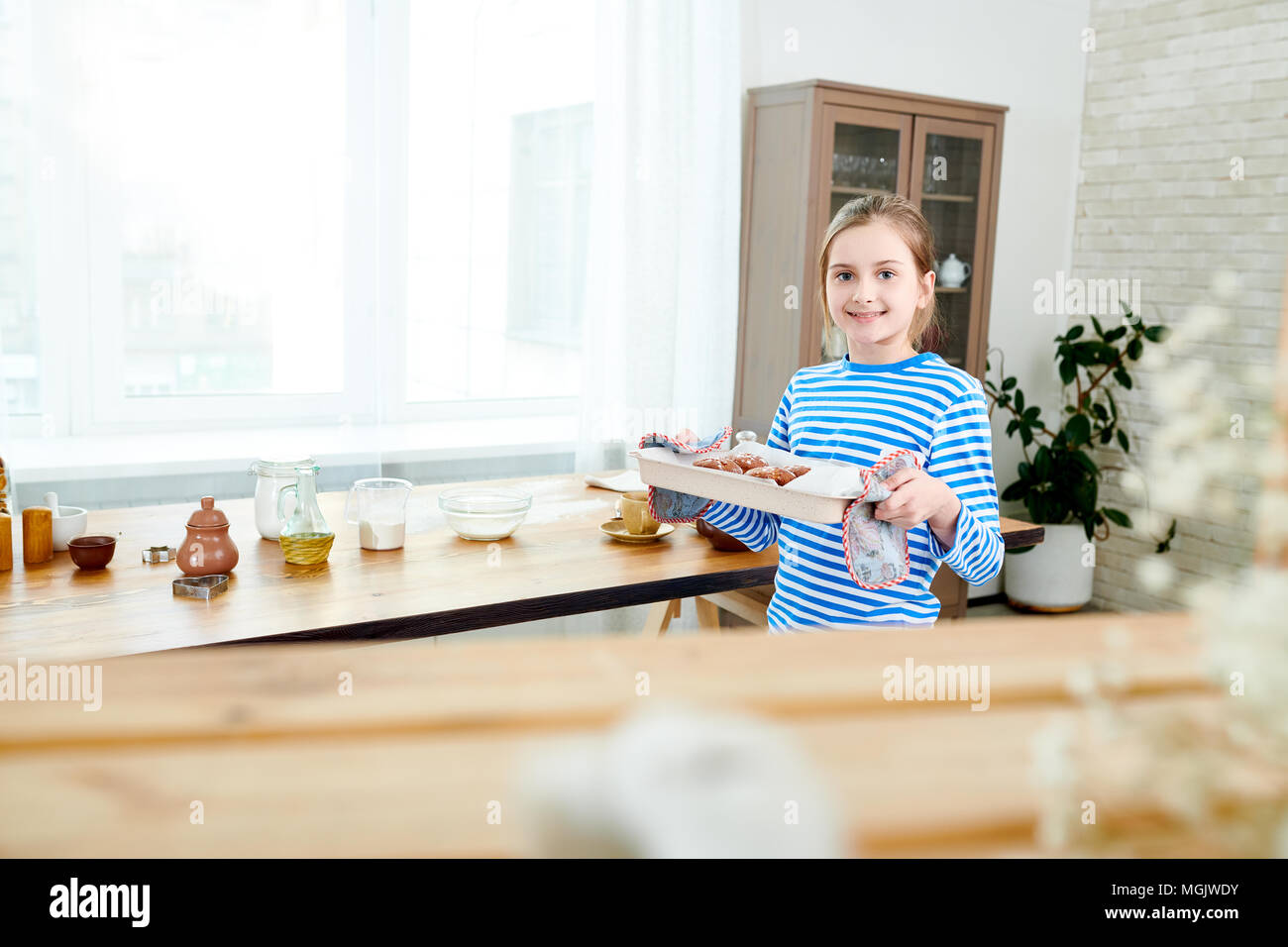 Ritratto di incantevole piccola ragazza con vassoio da forno con appena preparato tortine in mani e guardando la fotocamera mentre si effettua la sorpresa per la festa della mamma Foto Stock