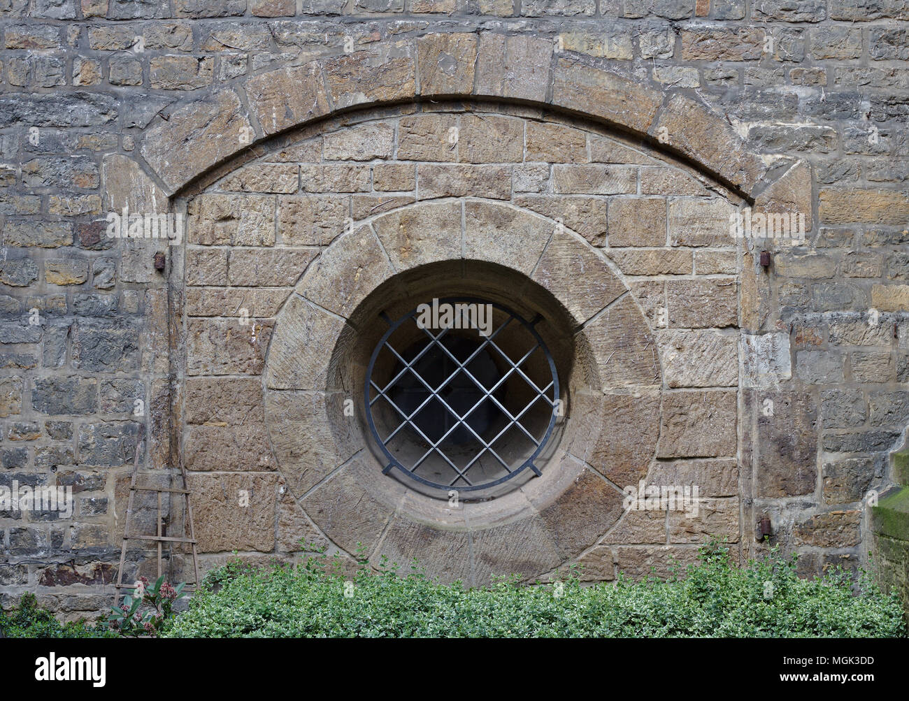 Antico muro di pietra arenaria con arco e bloccate finestra rotonda Foto Stock