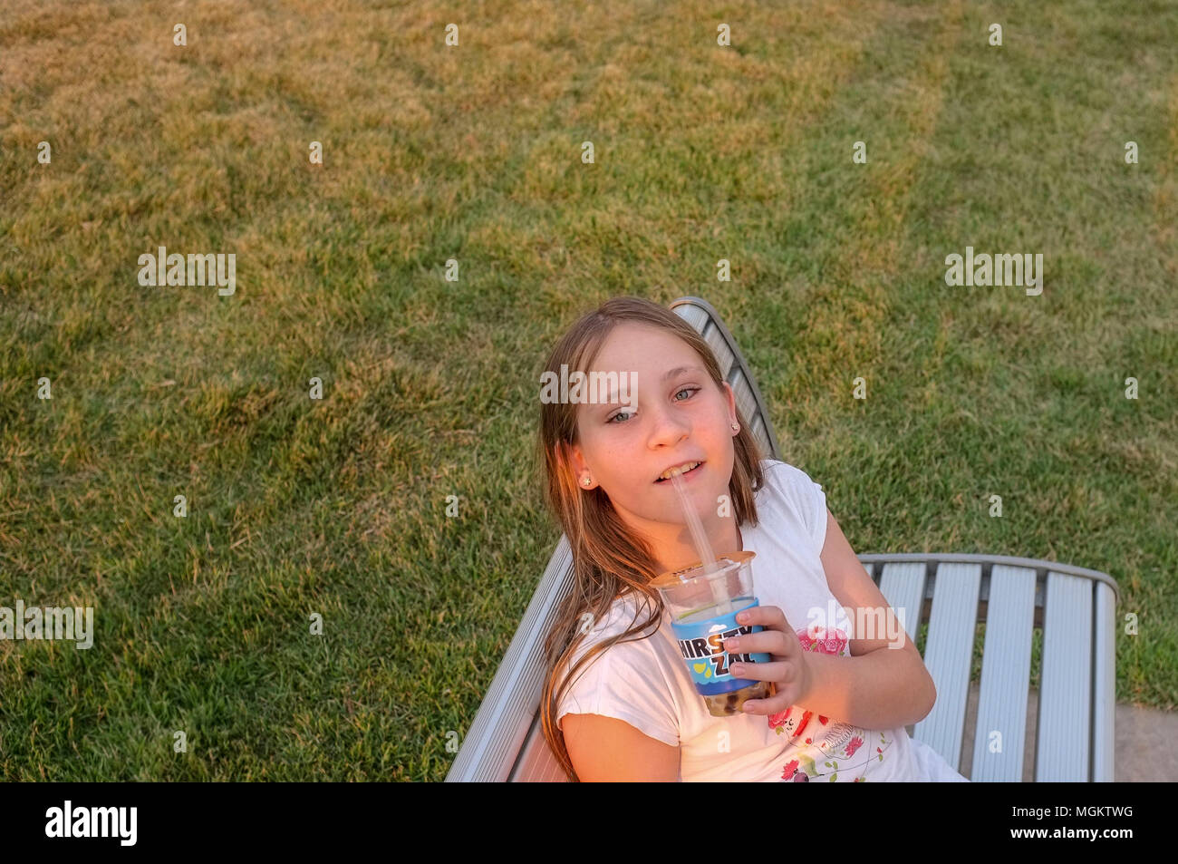 Giovane ragazza seduta su una panchina in un parco pubblico e di bere un take away drink, guardando la telecamera. Foto Stock