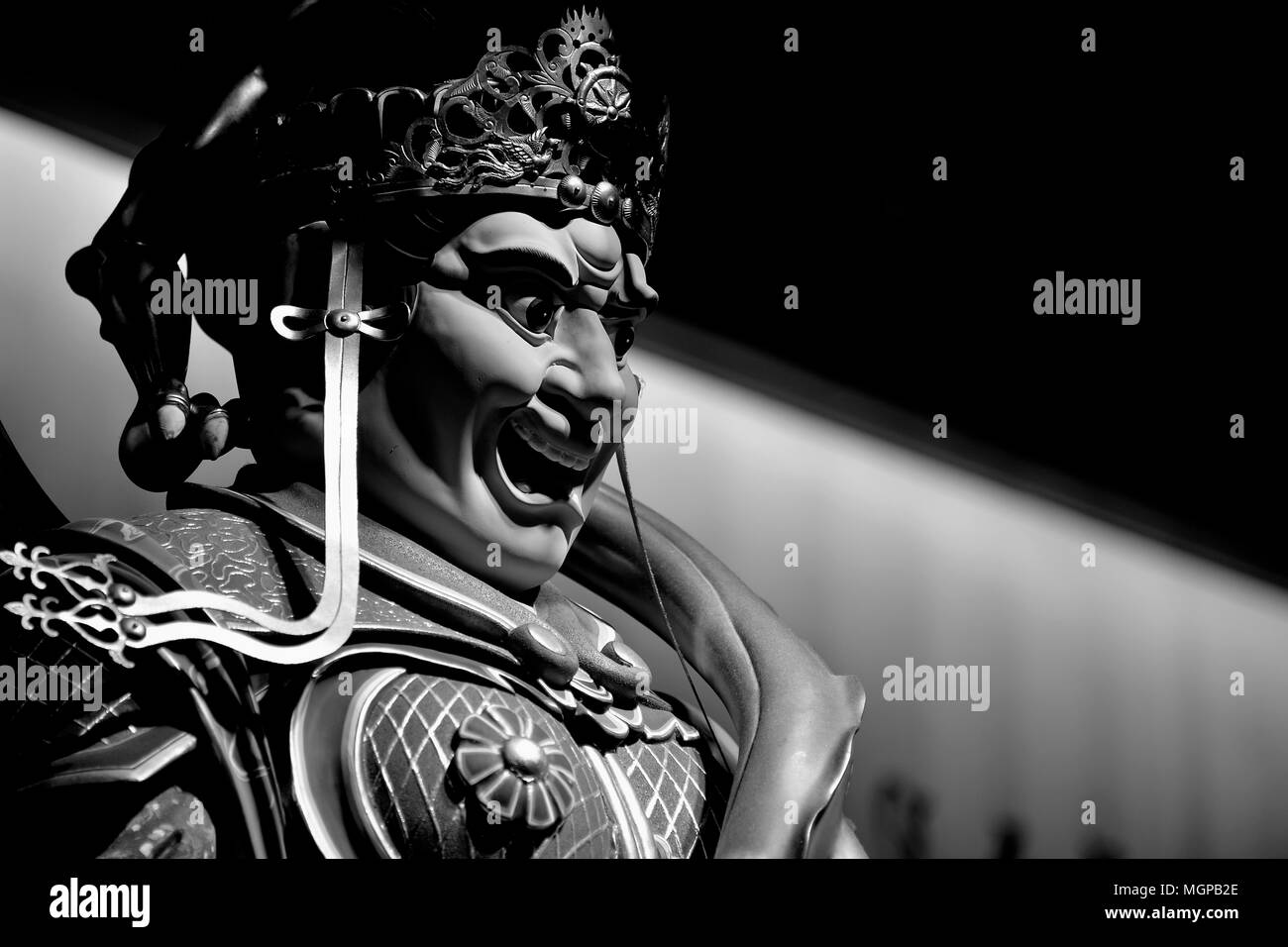 In prossimità della faccia di una statua di un feroce cinese tempio Buddista del tutore in monocromia con forti ombre Foto Stock