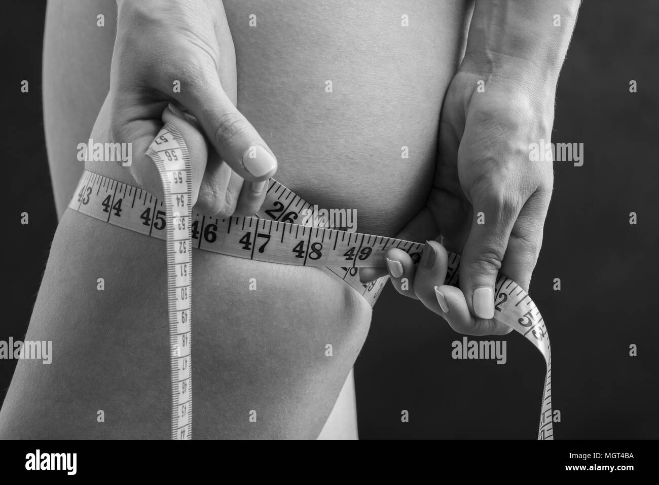 Triste giovane donna verificare la sua anca fat con nastro, monocromatico Foto Stock