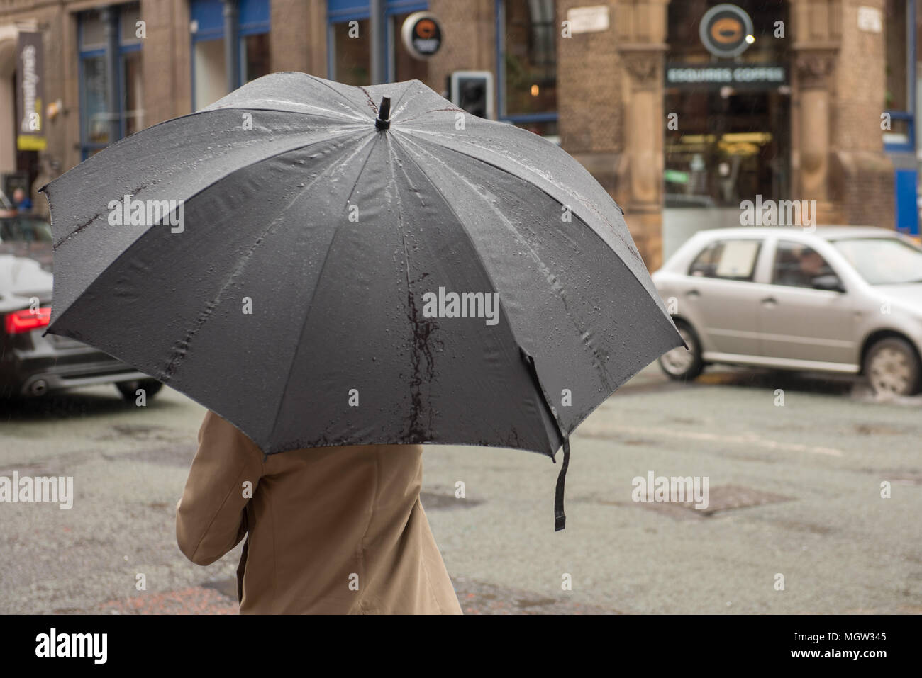 Persona al riparo sotto un grande ombrello nero in una strada piovosa fuori da una filiale del caffè Nero nel centro di Manchester, in Inghilterra Foto Stock