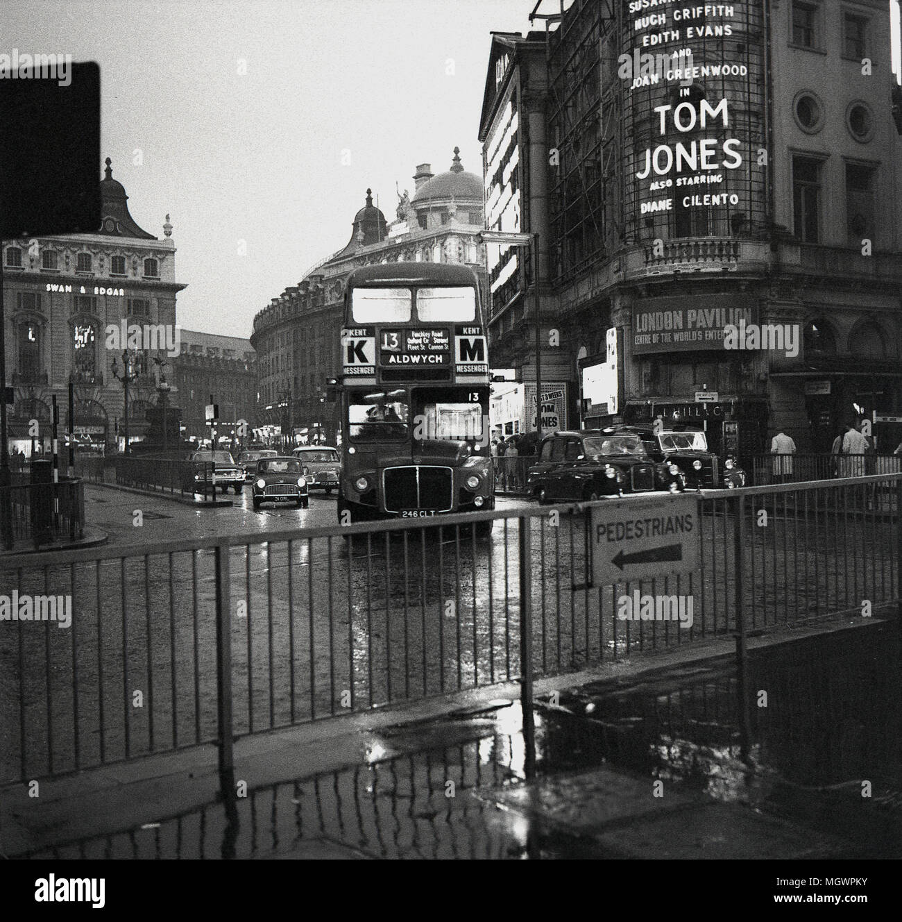 1963, immagine storica, Piccadilly Circus, Westminster, Londra, Inghilterra, su un umido umido di prima sera, un autobus routemaster sul raccordo stradale insieme ad altri mezzi di trasporto che arrivano da Regent Street. Un cartellone pubblicitario per il film, 'Tom Jones', si può vedere sulla destra della foto. Una commedia britannica, il film, un adattamento del romanzo di Henry Fielding del 1749, interpretato da Albert Figney, è stato sia un box Office che un successo critico. Foto Stock