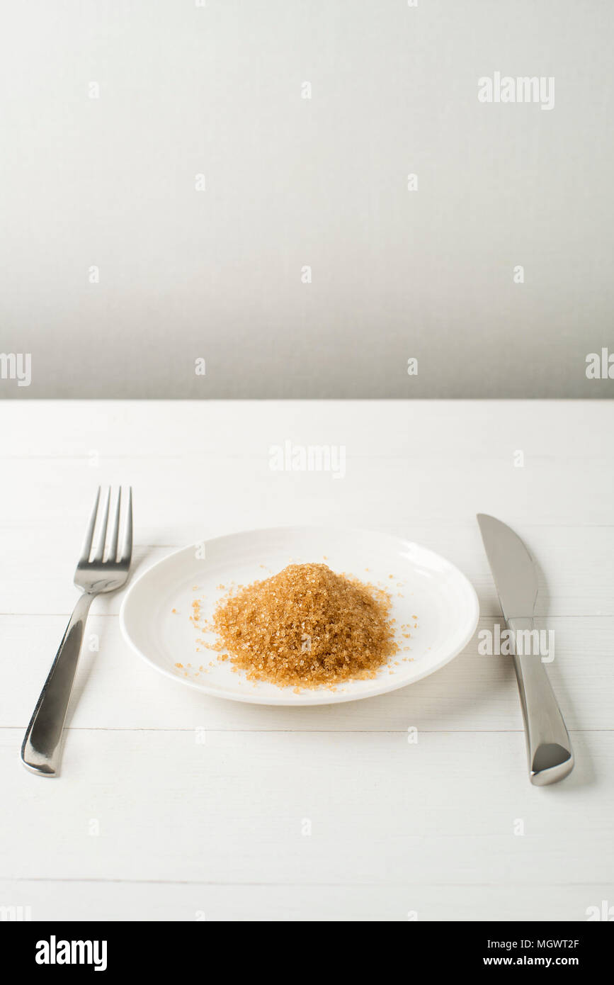 Lo zucchero Junk-Cibo, dieta e malsano mangiare concetto - close up di zucchero sulla piastra con coltello e forchetta. Cibo sano concetto, presentazione di zucchero conte Foto Stock