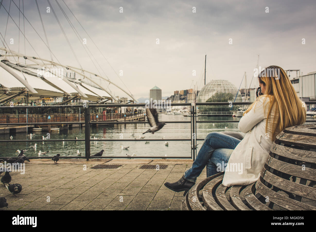 Ritratto di una giovane donna seduta e di scattare una foto di uccelli. Città, acqua e cielo in background Foto Stock