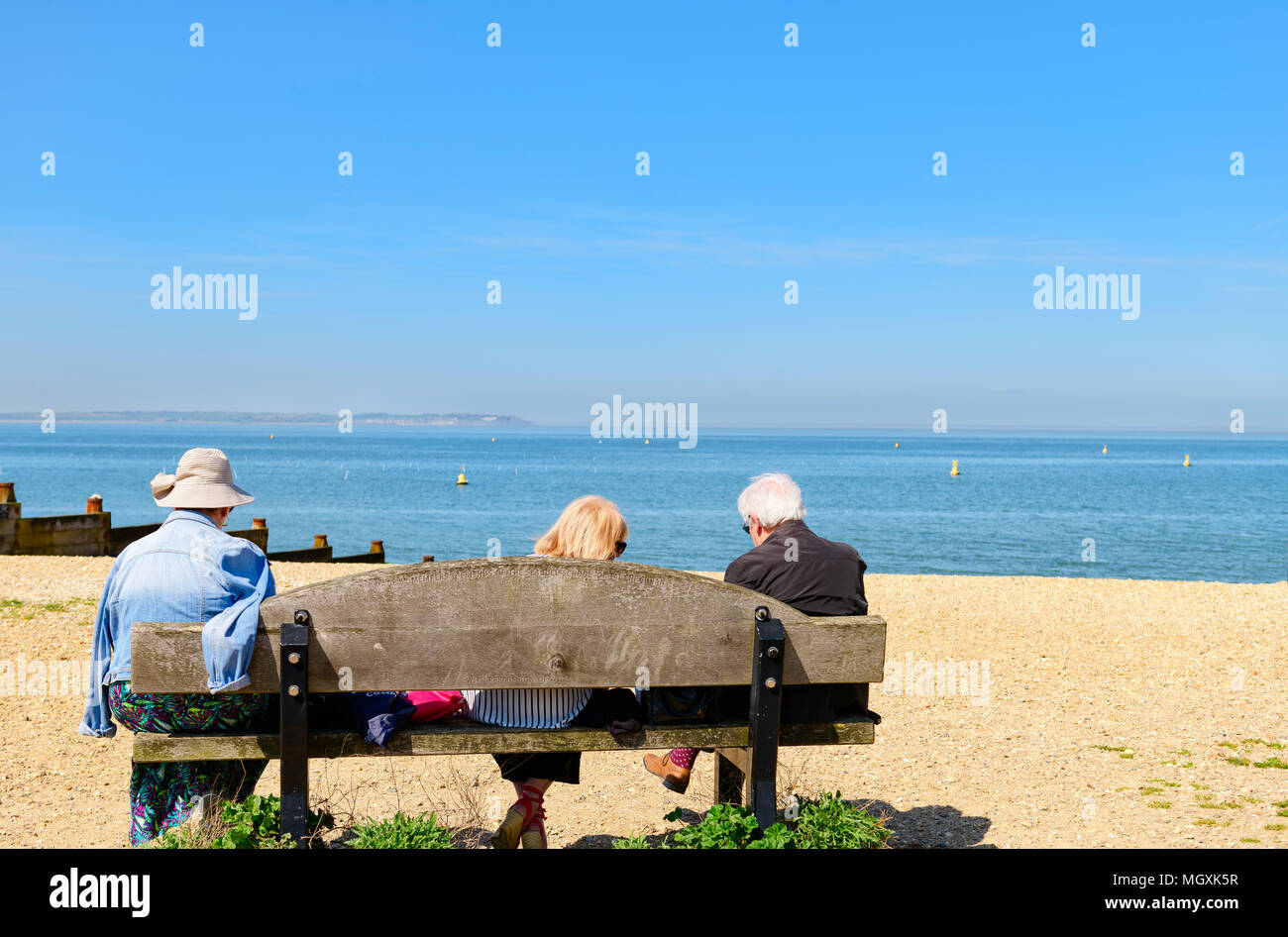 Gruppo di gente seduta su una panchina in riva al mare, Whitstable Kent Foto Stock