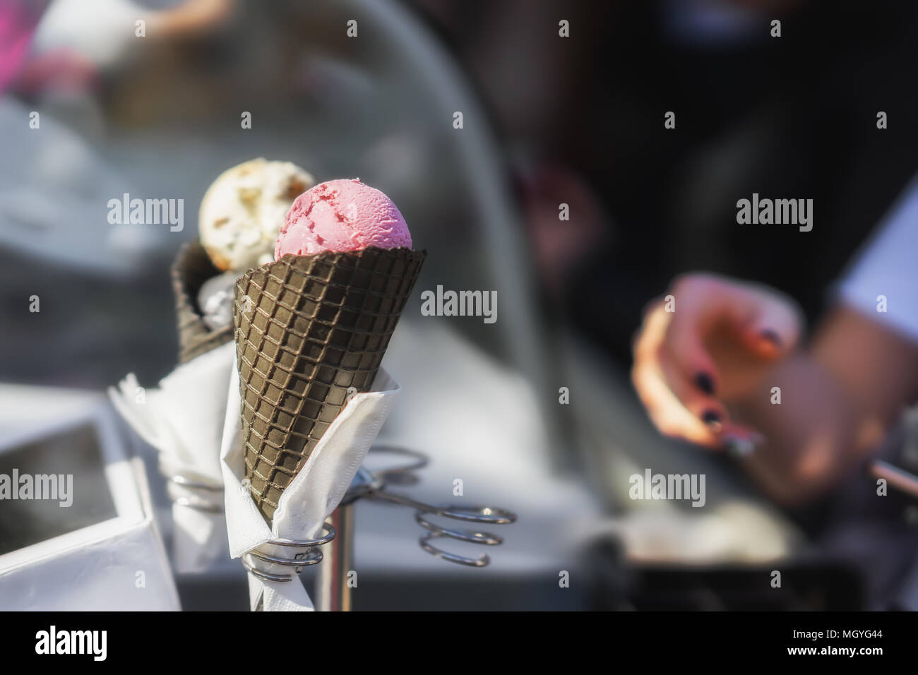 Due gustosi colorati coni gelato. Donna di mano richiede freschi e deliziosi gelati in cono nero, nuovo gusto dal supporto per gelati. Scena reale nel Foto Stock