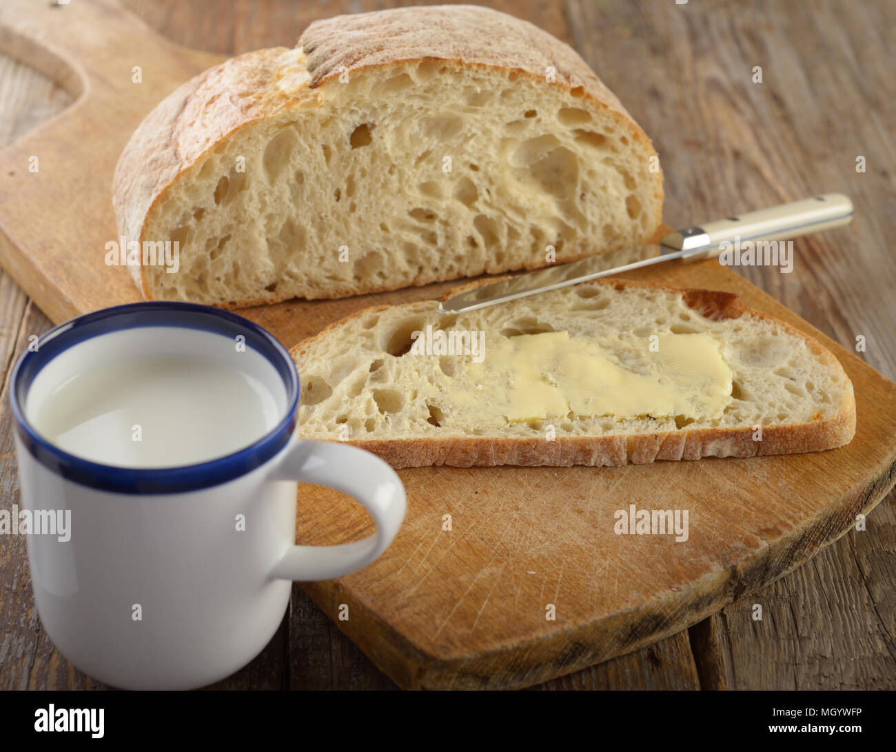 Pane con burro su un rustico tagliere e una tazza di latte Foto Stock