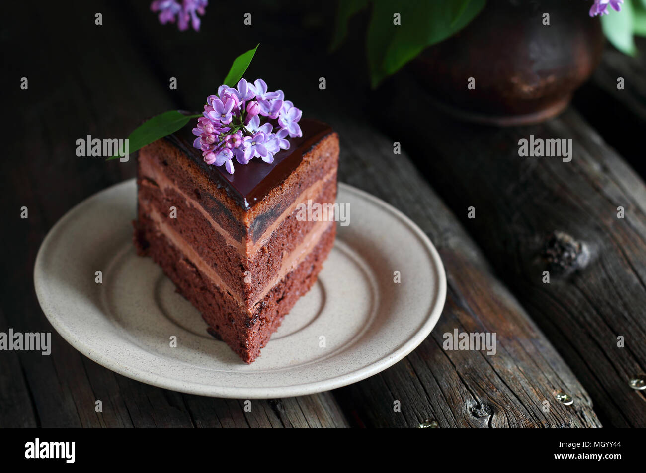 Pezzo di torta al cioccolato casalinga decorata con lillà su uno sfondo di legno Foto Stock