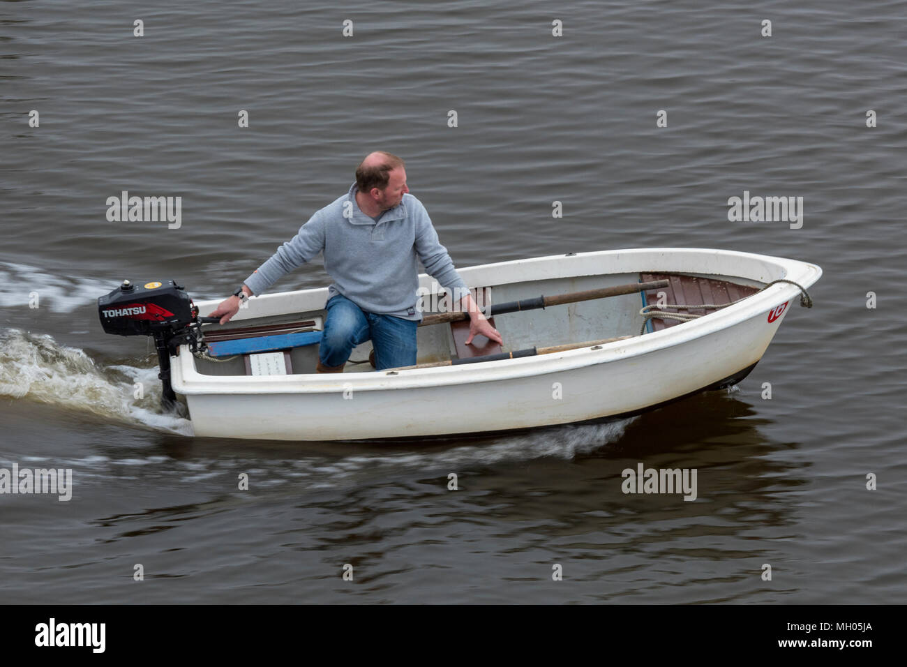 Un uomo con una piccola barca a remi o bando di gara per uno yacht con un motore fuoribordo essendo usati per guidare l'imbarcazione. Un uomo di mezza età in una piccola barca helming. Foto Stock