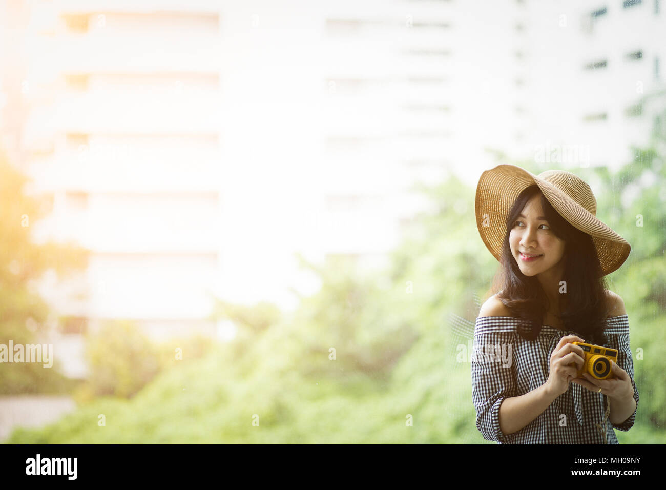 Ritratto di donna asiatica che indossa un cappello di paglia e guardando la luce del sole sulla sinistra. Fotografia di viaggiatori hipster lifestyle tenere la fotocamera in roo Foto Stock
