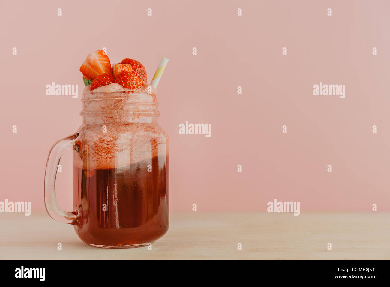Vaso di vetro con colore rosso brillante limonata fatta di fragole guarnito con frutti di bosco e servite con paglia in rosa. Foto Stock