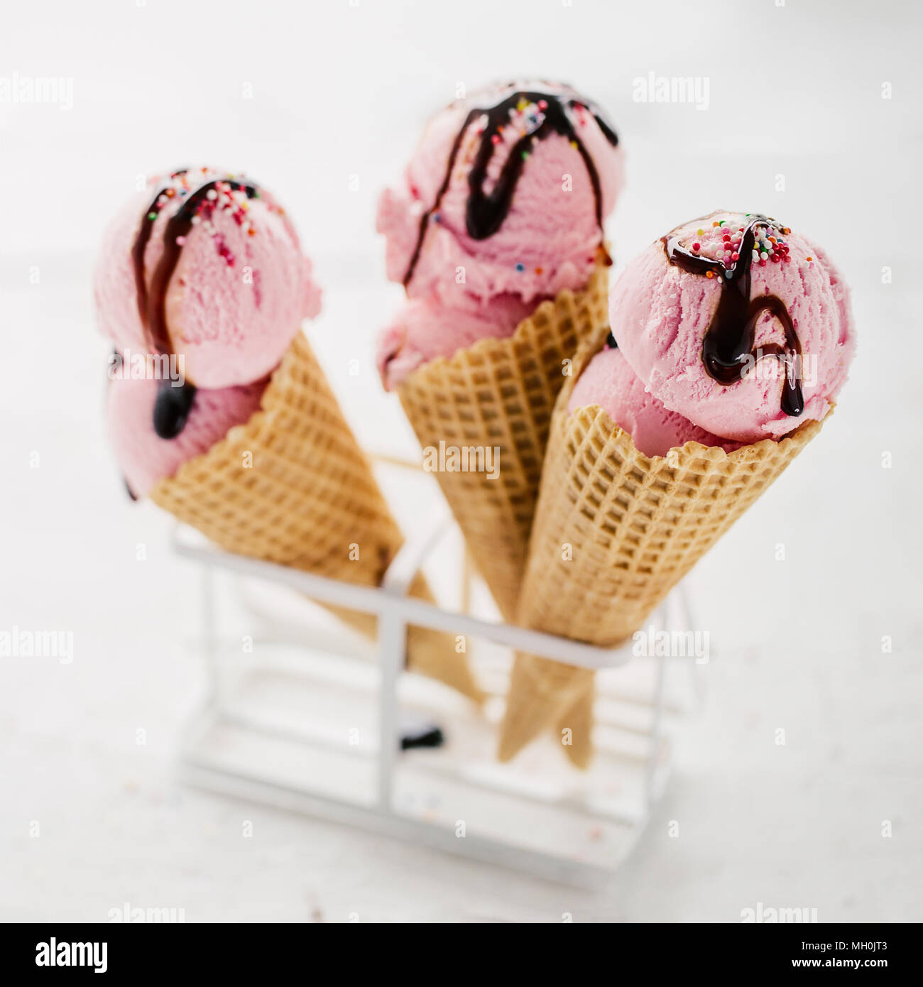 Pochi i coni di cialda riempiti con rosa di gelati e servita con cioccolato topping e spruzza. Foto Stock