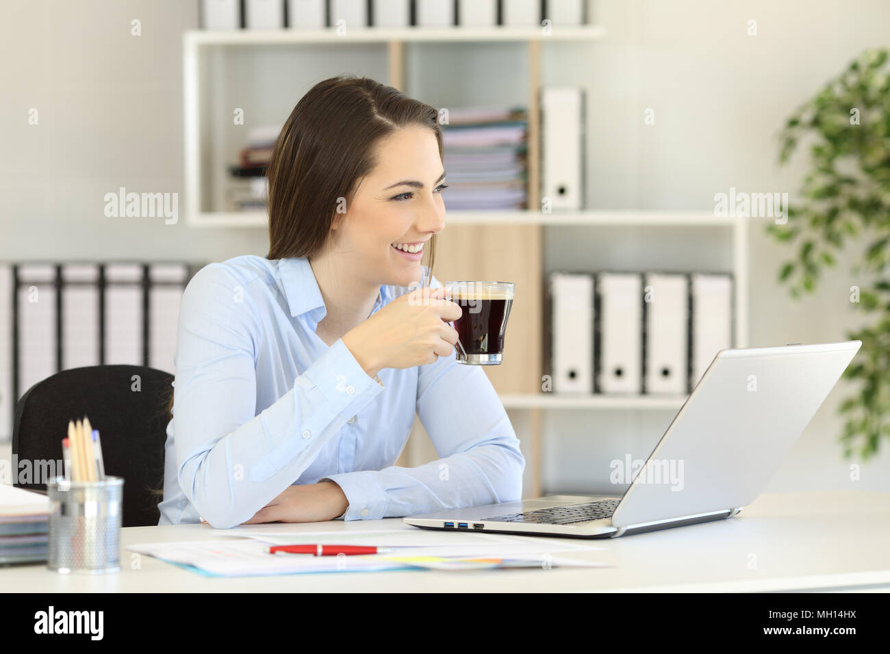 Felice lavoratore di ufficio avente una pausa caffè guardando lontano e sorridente Foto Stock