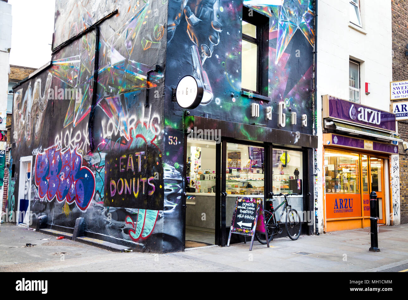 Edificio coperto di street art graffiti, facciata di Magna donut shop in Brick Lane, London, Regno Unito Foto Stock
