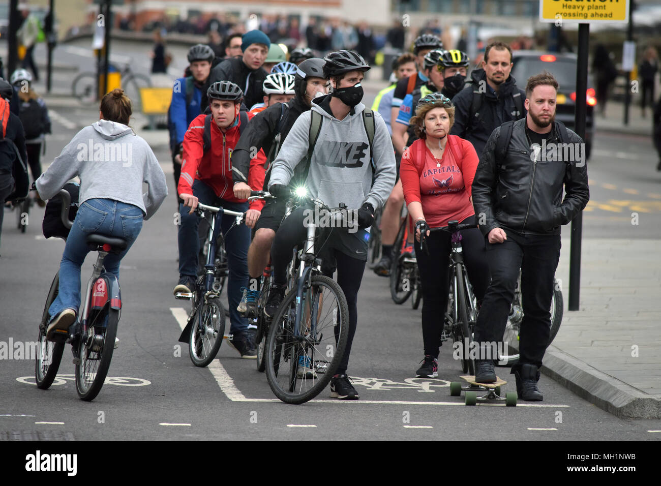 I ciclisti che indossano maschere al viso e un guidatore di skateboard di attendere presso la giunzione del traffico su Blackfriars Bridge e Stamford Street in direzione sud verso Southwark Foto Stock