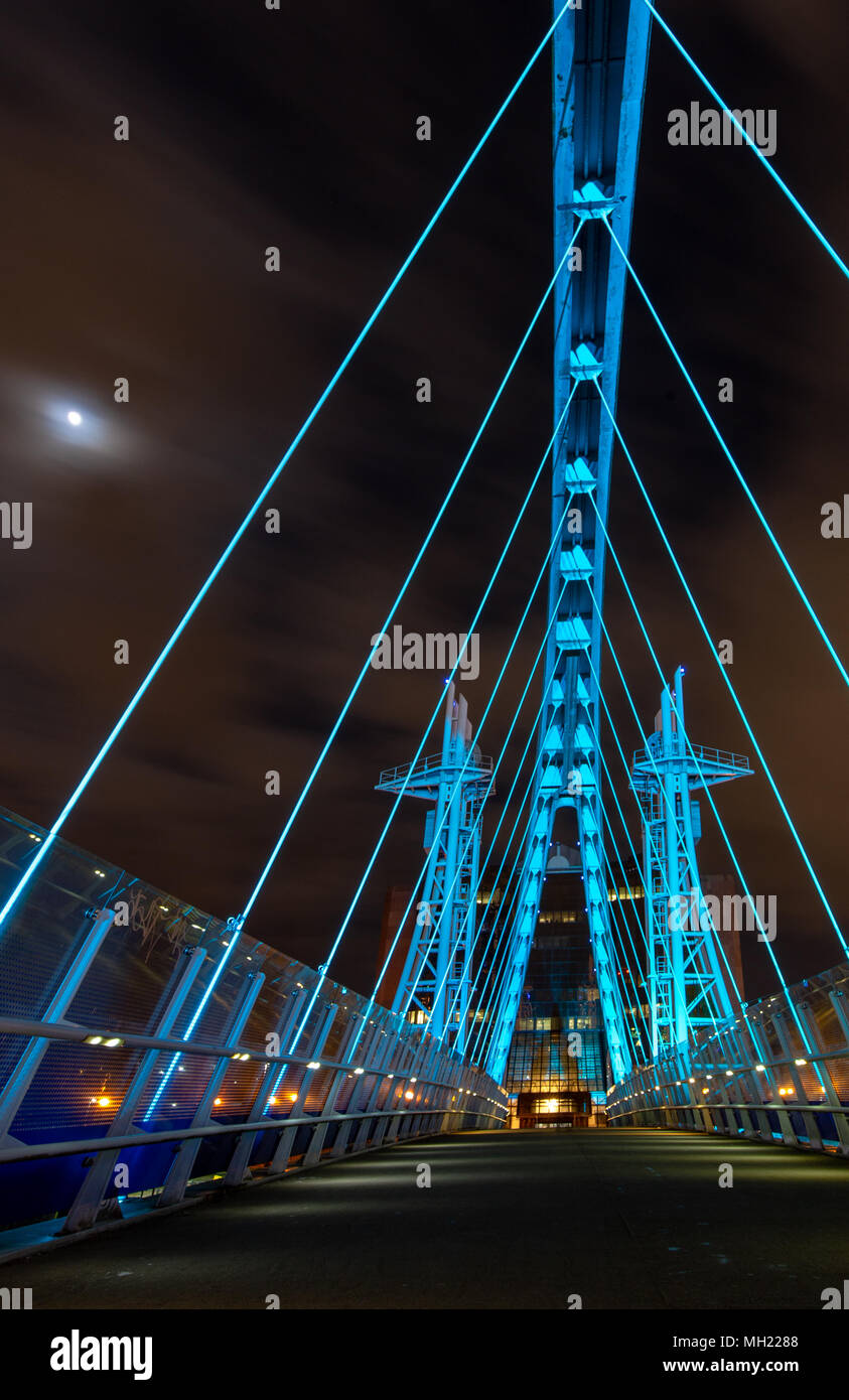 Il Lowry (Millenium) e sollevare il ponte pedonale illuminato con illuminazione blu durante la notte e la luna proveniente attraverso le nuvole. Preso il 26 aprile 2018. Foto Stock