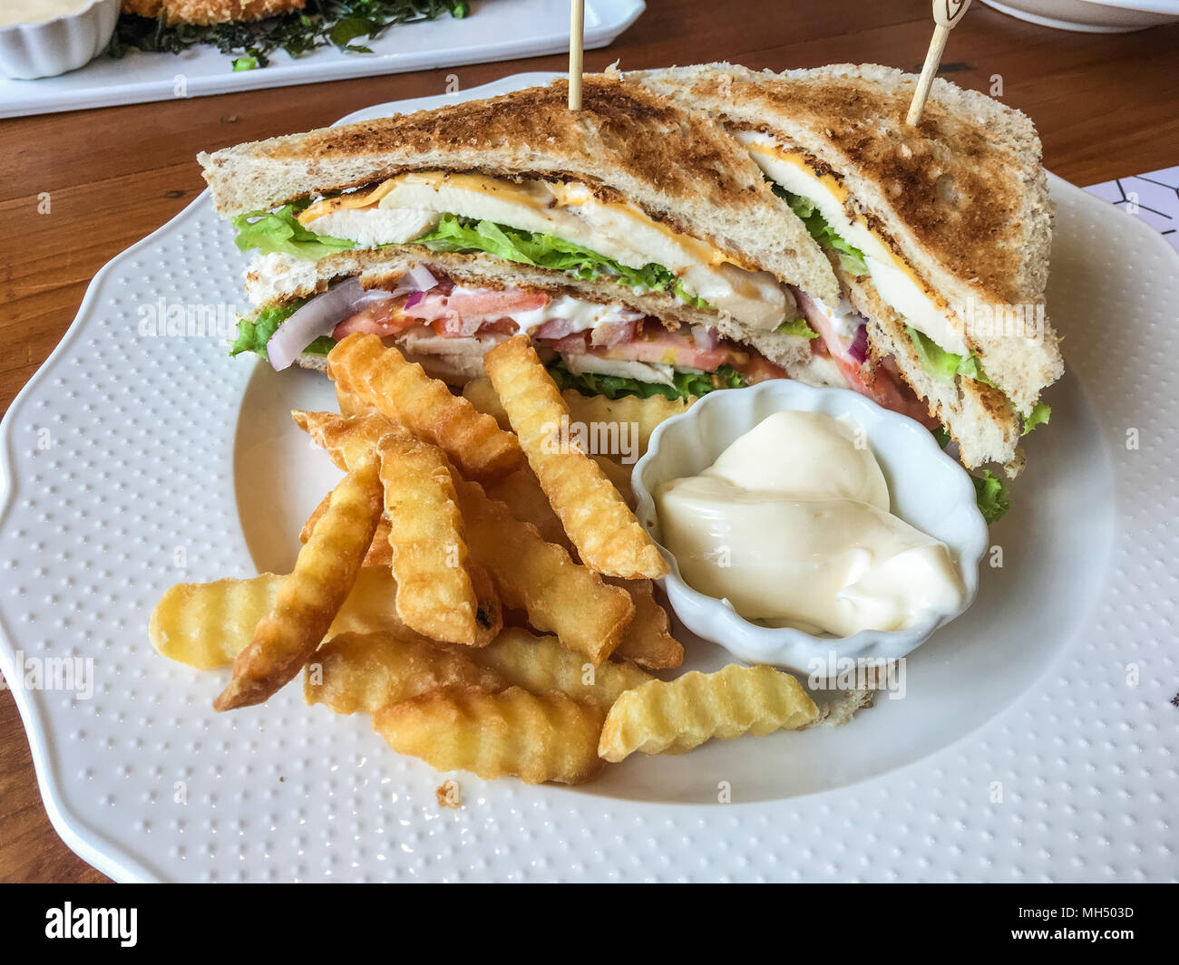 Sandwich di pollo e patatine fritte con salsa maionese sulla piastra bianca al ristorante. Foto Stock