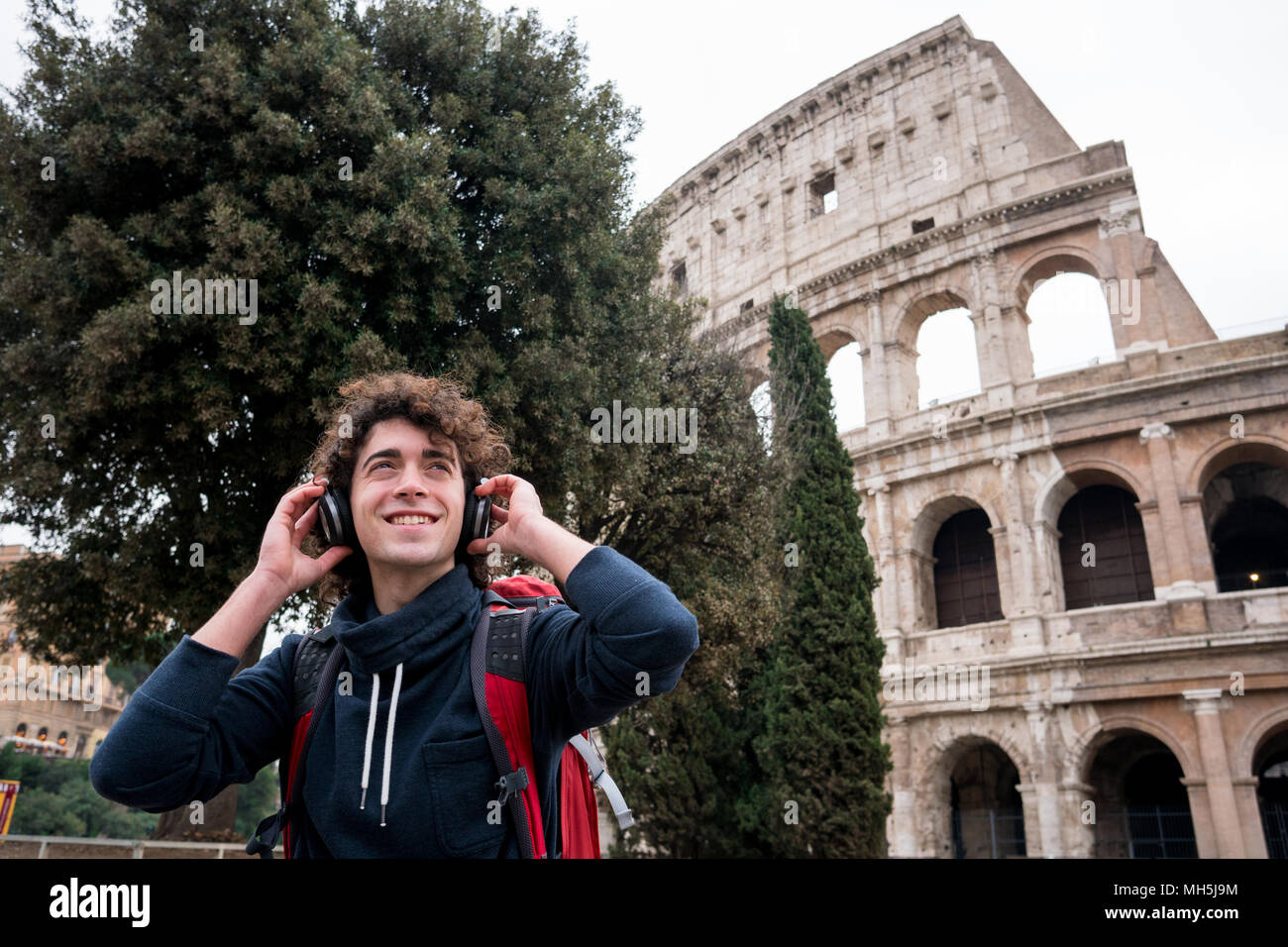 Bel giovane con le cuffie per ascoltare musica davanti al Colosseo a Roma Foto Stock
