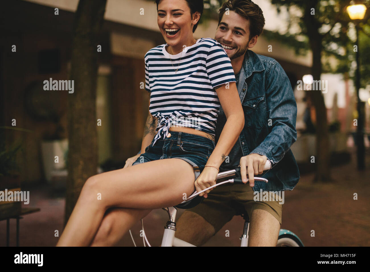 Uomo Bicicletta Equitazione con la sua ragazza seduta sul manubrio. Giovane avendo divertimento mentre la bicicletta equitazione. Foto Stock
