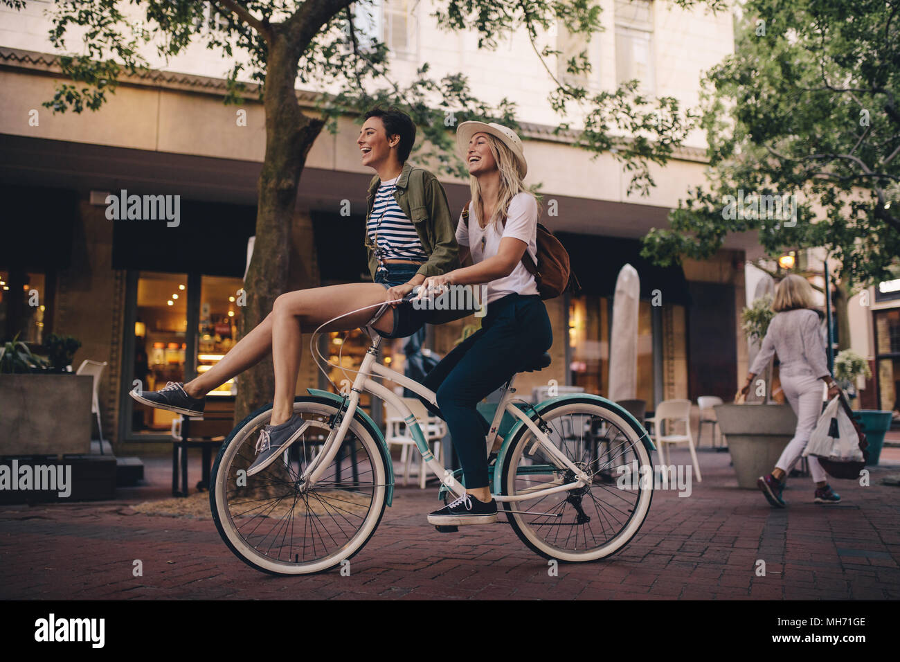 Donna sorridente seduto sul manubrio di una bicicletta con il suo amico. Belle  Donne godendo in bicicletta in città Foto stock - Alamy