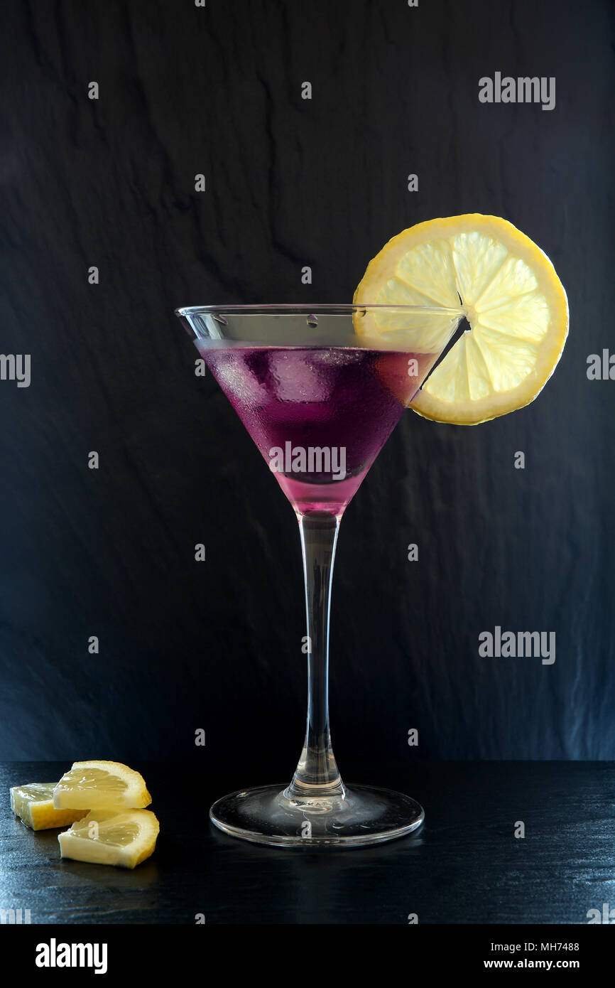 Estate Fresca Purple Rain il cocktail in una coppetta Martini con le fette di limone su un nero superficie testurizzata Foto Stock
