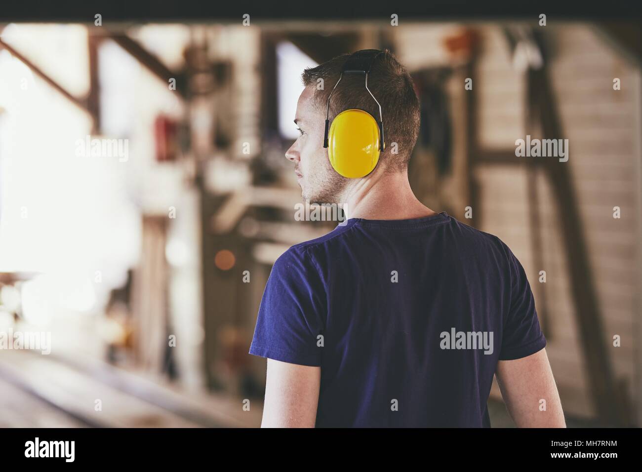 Uomo che lavora in segheria. Vista posteriore del lavoratore con auricolare. Foto Stock