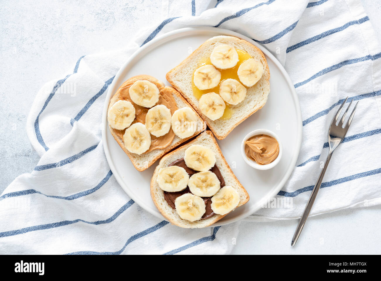 Banana Burro di arachidi toast sulla piastra bianca. Vegan Snack o la prima colazione. Dado di deliziosi burro, pane e fette biscottate di Banana. Mangiare sano, uno stile di vita sano Foto Stock