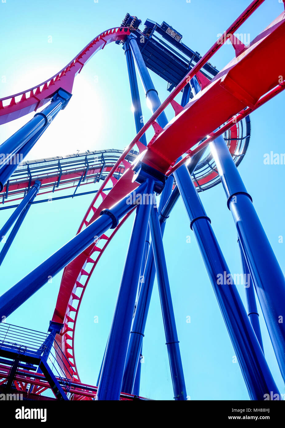 Cerca fino al metallo alta blu e rosso di lavoro del telaio di un moderno ed alto rollercoaster formando delle forme grafiche e delle linee, cielo blu e blu piscina, rullo Foto Stock