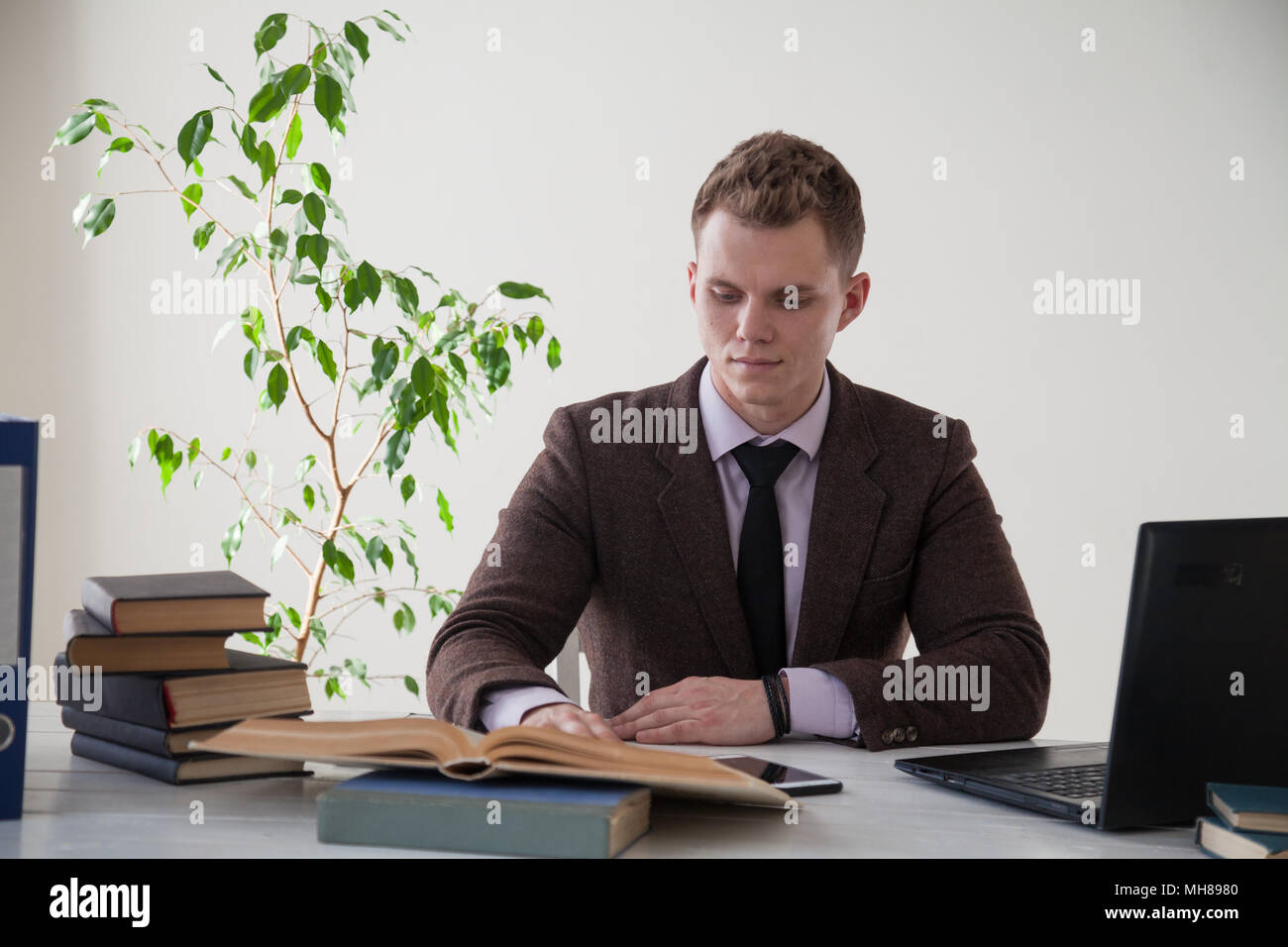 Un uomo in un business suit lavora al computer con libri in ufficio Foto Stock