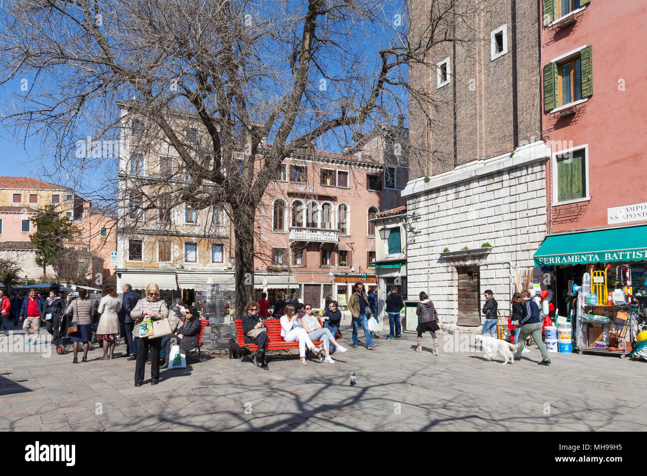 Local veneziani godendo il sole primaverile Campo Santi Apostoli, Cannaregio, Venezia, Italia seduti sui banchi, lo shopping e le passeggiate di un cane Foto Stock