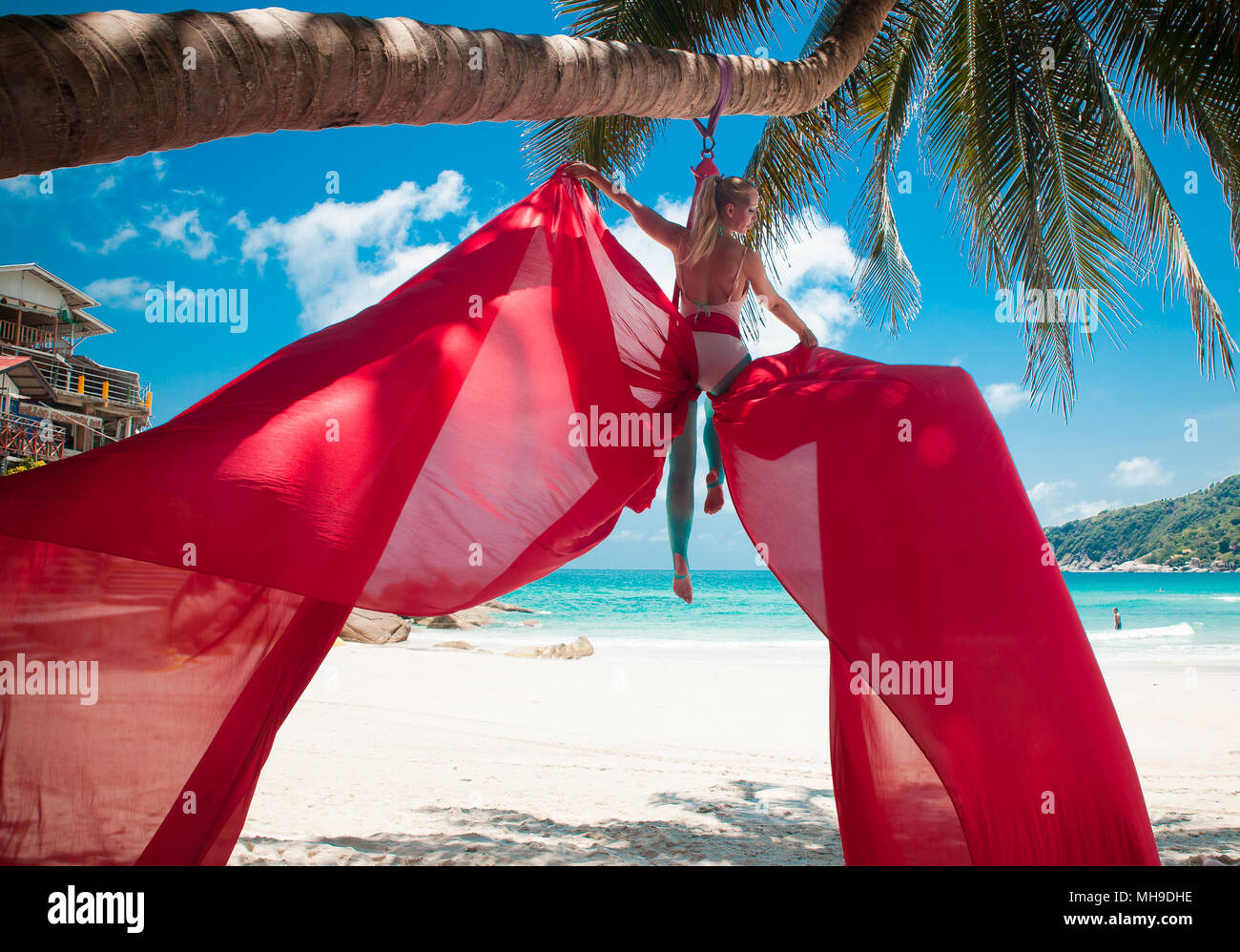 Femmina facendo trapezista acrobatici volteggi con un rosso sete dell'antenna su una spiaggia in un ambiente tropicale. Foto Stock