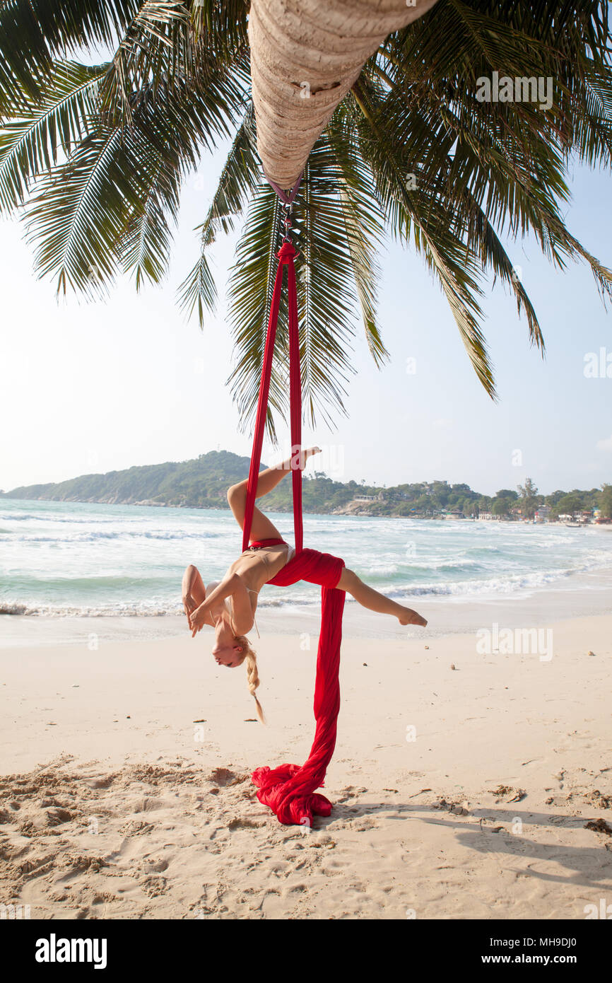 Femmina facendo trapezista acrobatici volteggi con un rosso sete dell'antenna su una spiaggia in un ambiente tropicale. Foto Stock