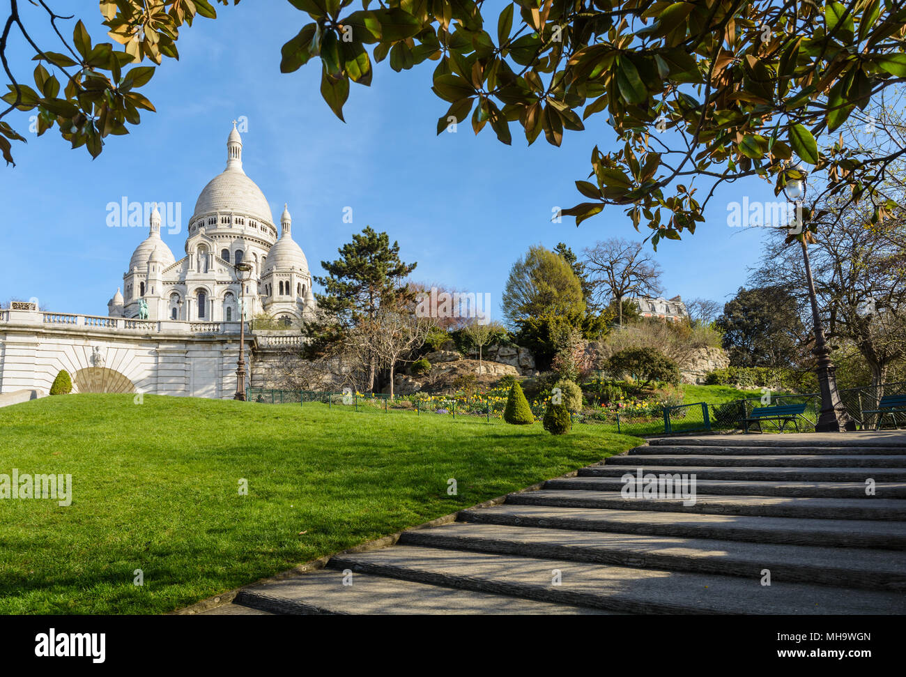 La basilica del Sacro Cuore di Parigi in cima alla collina di Montmartre visto da Louise Michel park con fogliame e scale in primo piano Foto Stock