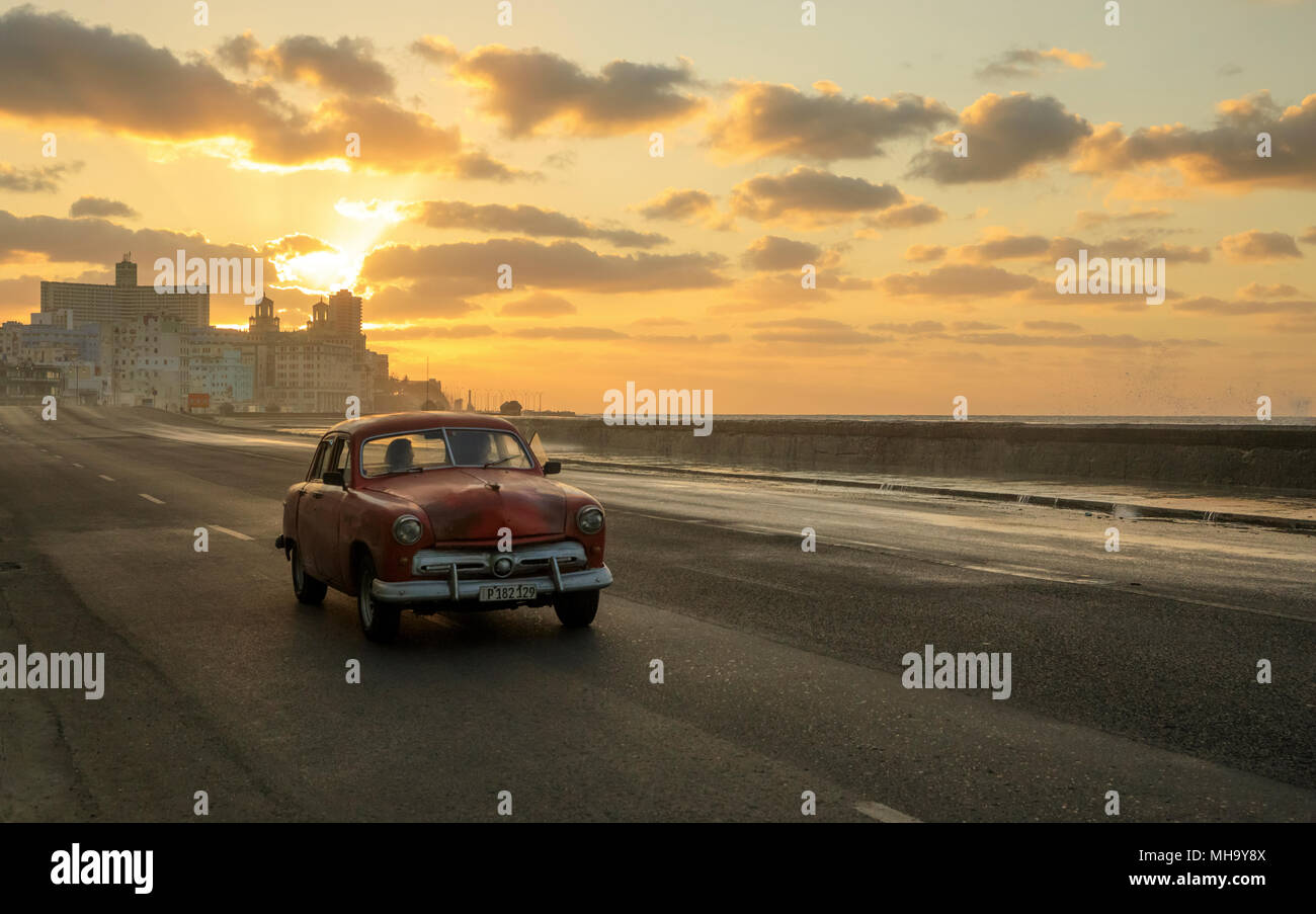 Onde infrangersi come il sole tramonta come classic cars corsa lungo il Malecon a l'Avana, Cuba. Foto Stock