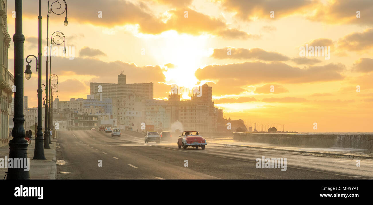 Il sole tramonta come classic cars corsa lungo il Malecon a l'Avana, Cuba. Foto Stock