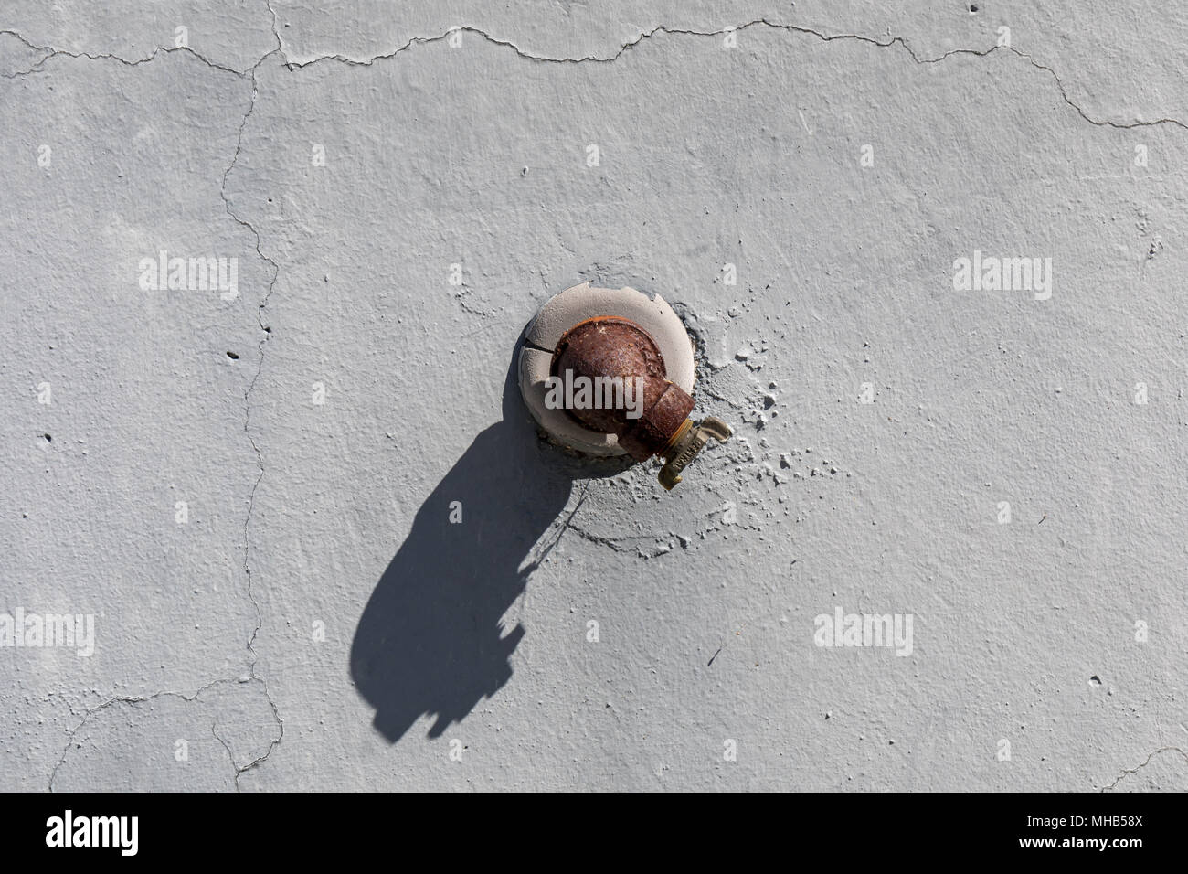 Valvola arrugginito getta un' ombra sulla parete da cui sporge Foto Stock